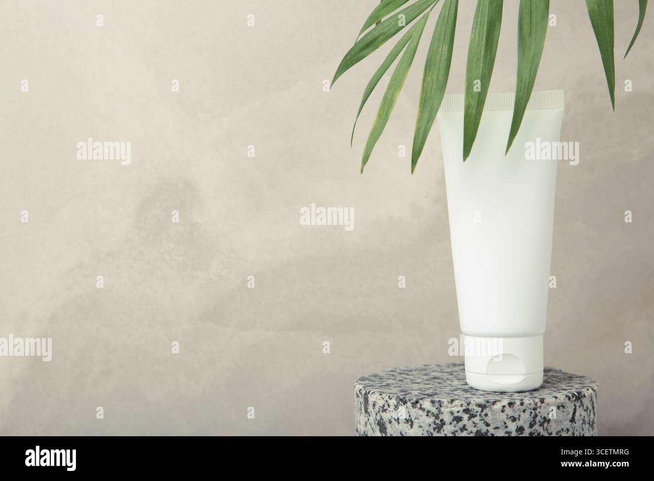 Weißes Kosmetikröhrchen mit grünen Blättern auf hellgrauem Hintergrund. Mockup für das Branding von Kosmetikprodukten. Stockfoto