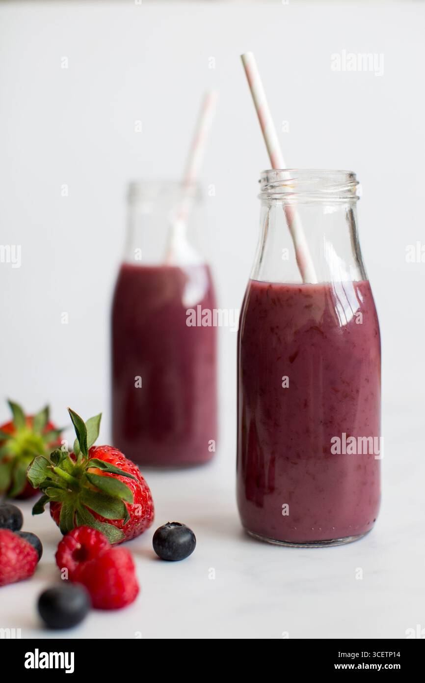 Beeren-Smoothie in Glasflaschen mit Papierhalmen und frischen Erdbeeren, Himbeeren und Heidelbeeren auf weißem Hintergrund. Stockfoto
