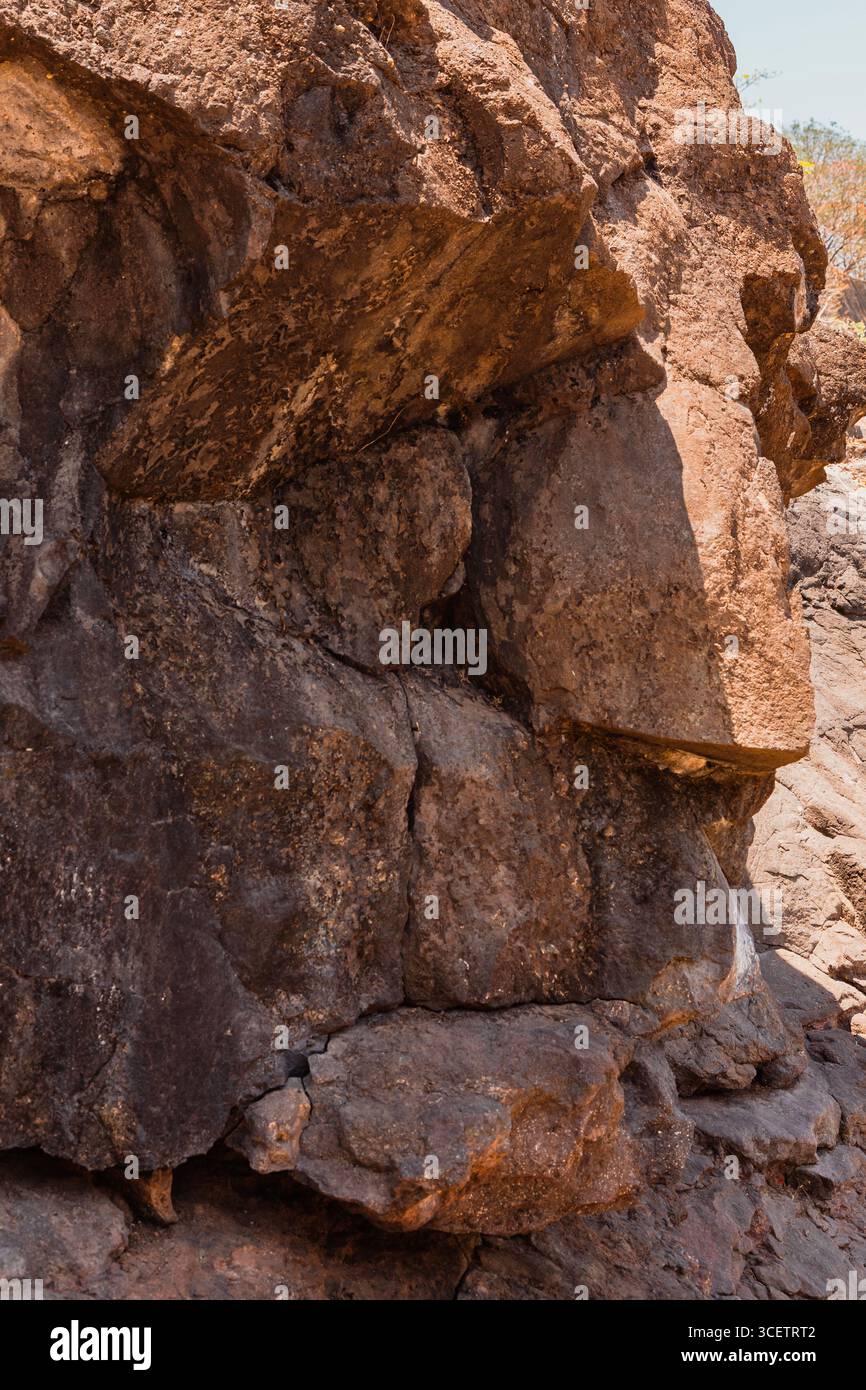 Nahaufnahme von rauen, verwitterten braunen Felsformationen mit ungleichmäßigen Texturen und natürlichem Sonnenlicht, das die Oberflächendetails hervorhebt. Stockfoto