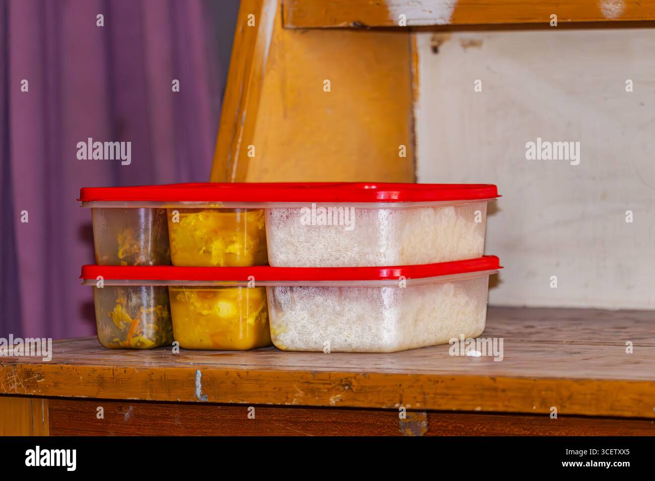 Frisch gepackte hausgemachte Mahlzeit für das Hostel mit Reis und Curry in Plastikkisten mit rotem Deckel auf Holztisch Stockfoto