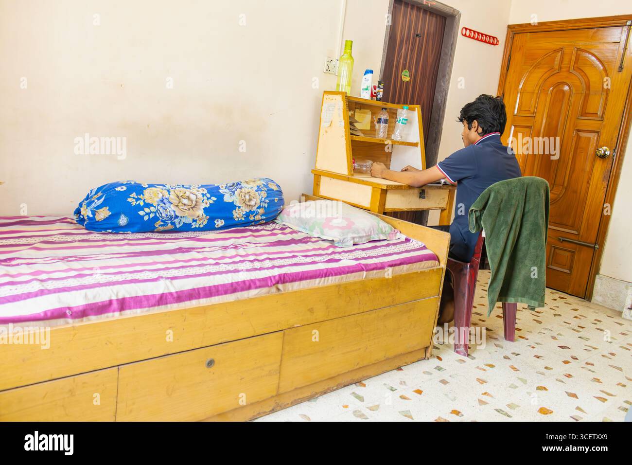 Ernsthafter Student, der neben einem ordentlich gehaltenen Bett in einem kleinen Hostel-Zimmer an Notizen arbeitete Stockfoto