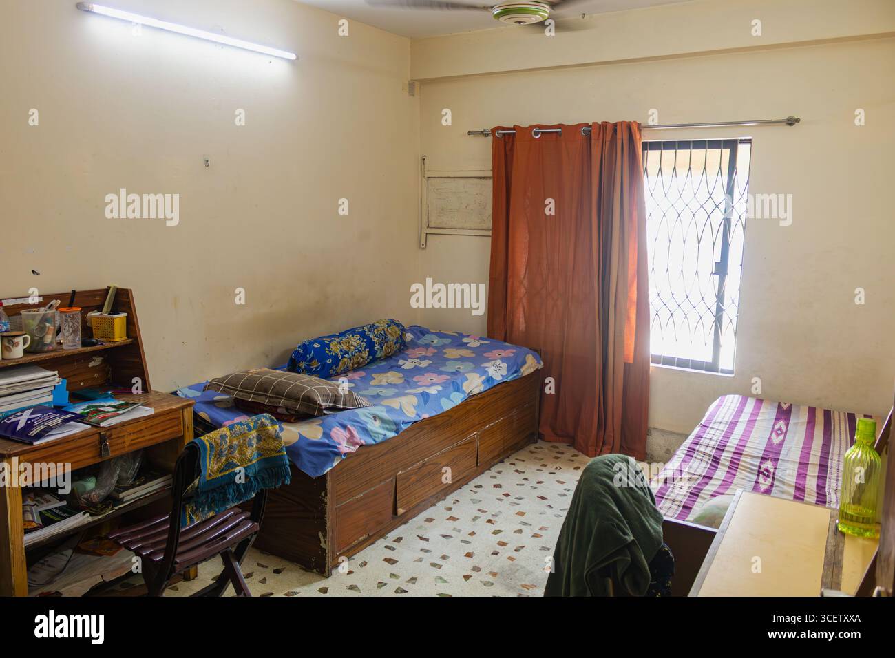 Organisierter Studentenarbeitsplatz mit Holzschreibtisch, Lernmaterialien und Bett vor hell bemalten Wänden. Stockfoto
