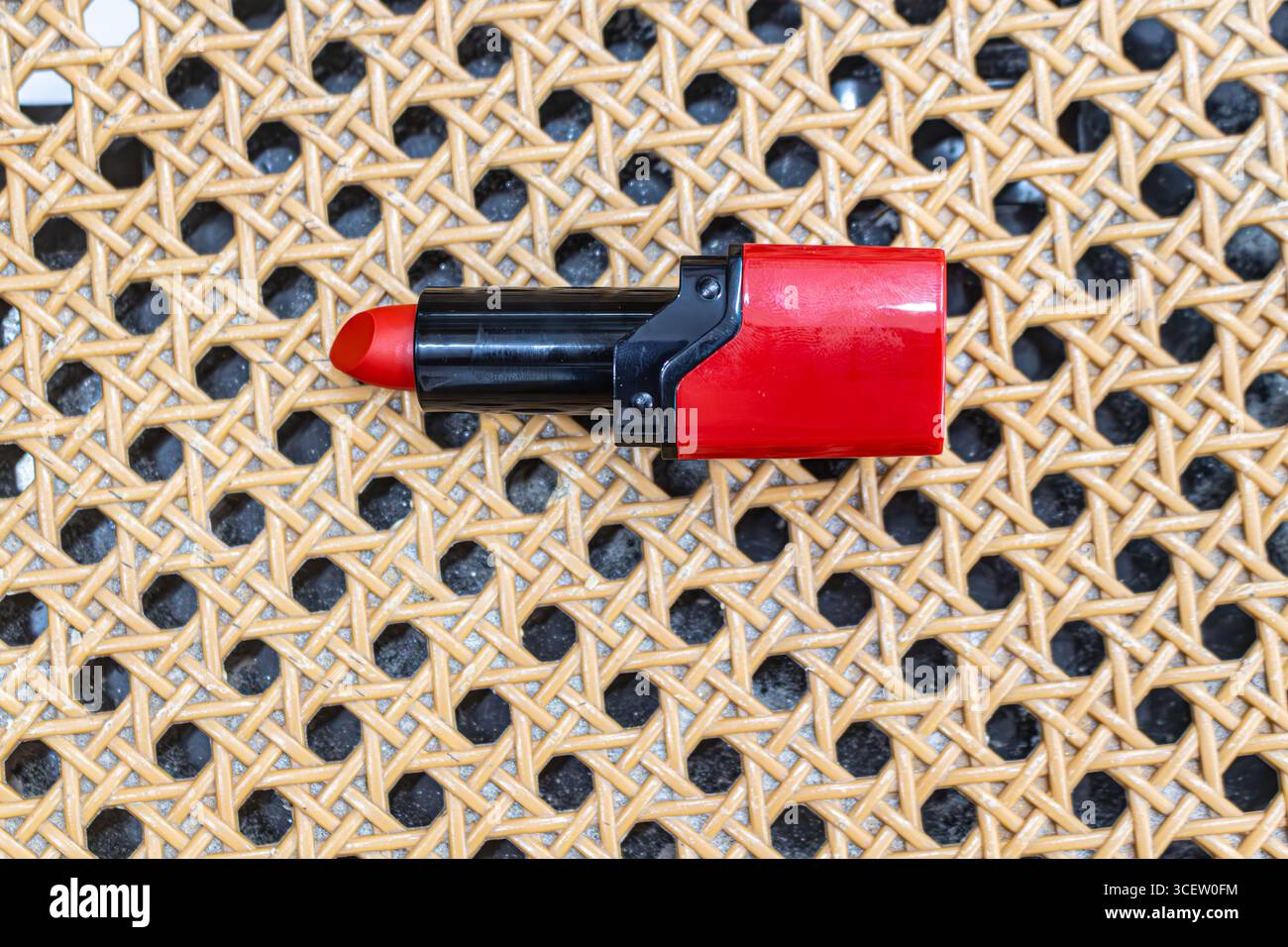 Leuchtend rote Lippenstiftröhre auf gewebter Rattan-Oberfläche mit auffälligem und elegantem Kosmetikdesign Stockfoto