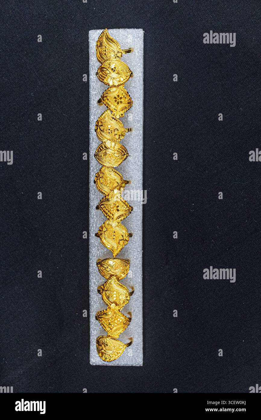 Elegante, dekorative Goldringe, die perfekt auf einem Schmuckhalter aus dunklem Schaumstoff angeordnet sind Stockfoto
