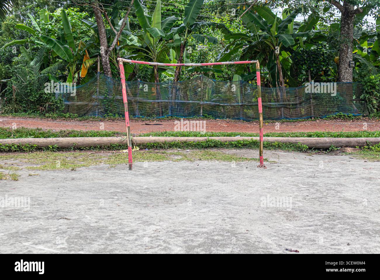 Leerer Sanddorfspielplatz mit kleinen handgefertigten Bambus-Torpfosten, umgeben von Bananenbäumen und grünem Zaun Stockfoto