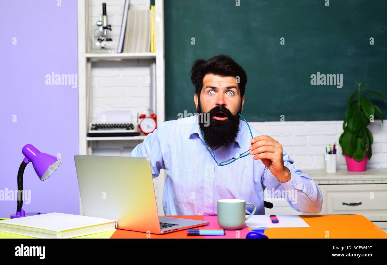 Überraschter Student, der sich auf die Prüfung oder Prüfung an der Universität vorbereitet. Männlicher Lehrer, der mit Laptop im Klassenzimmer arbeitet. Lernen, Bildung und Wissen. Gut Aussehend Stockfoto