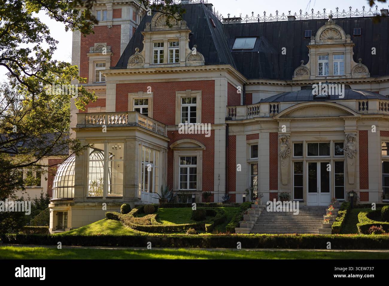 Gemütliches altes Herrenhaus umgeben von einem ruhigen Garten, warmes Sonnenlicht schafft romantische Atmosphäre auf der eleganten Fassade, einladende dekorative Details Stockfoto