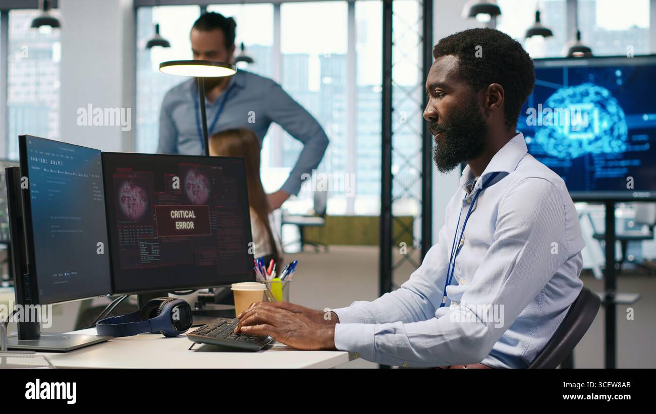 Programmierer im Büro, der Hilfe von Kollegen anfordert, um kritische Fehlerwarnungen zu beheben. IT-Mitarbeiter und Kollegen suchen nach Brainstorming, wie Computerfehler behoben werden können, die sich auf Systeme, Kamera A, auswirken Stockfoto