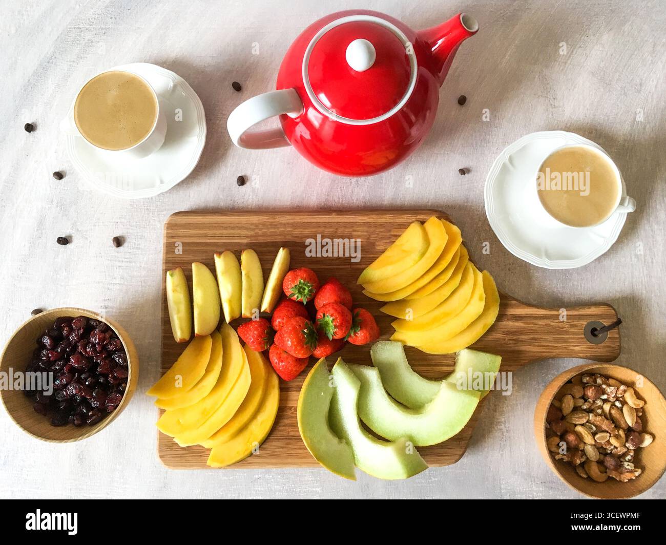 Blick von oben auf farbenfrohe gesunde, frische Snacks oder Frühstück. Kaffee, Tee, Mango, Melone, Erdbeeren, Äpfel, trockene Beeren und Nüsse. Stockfoto