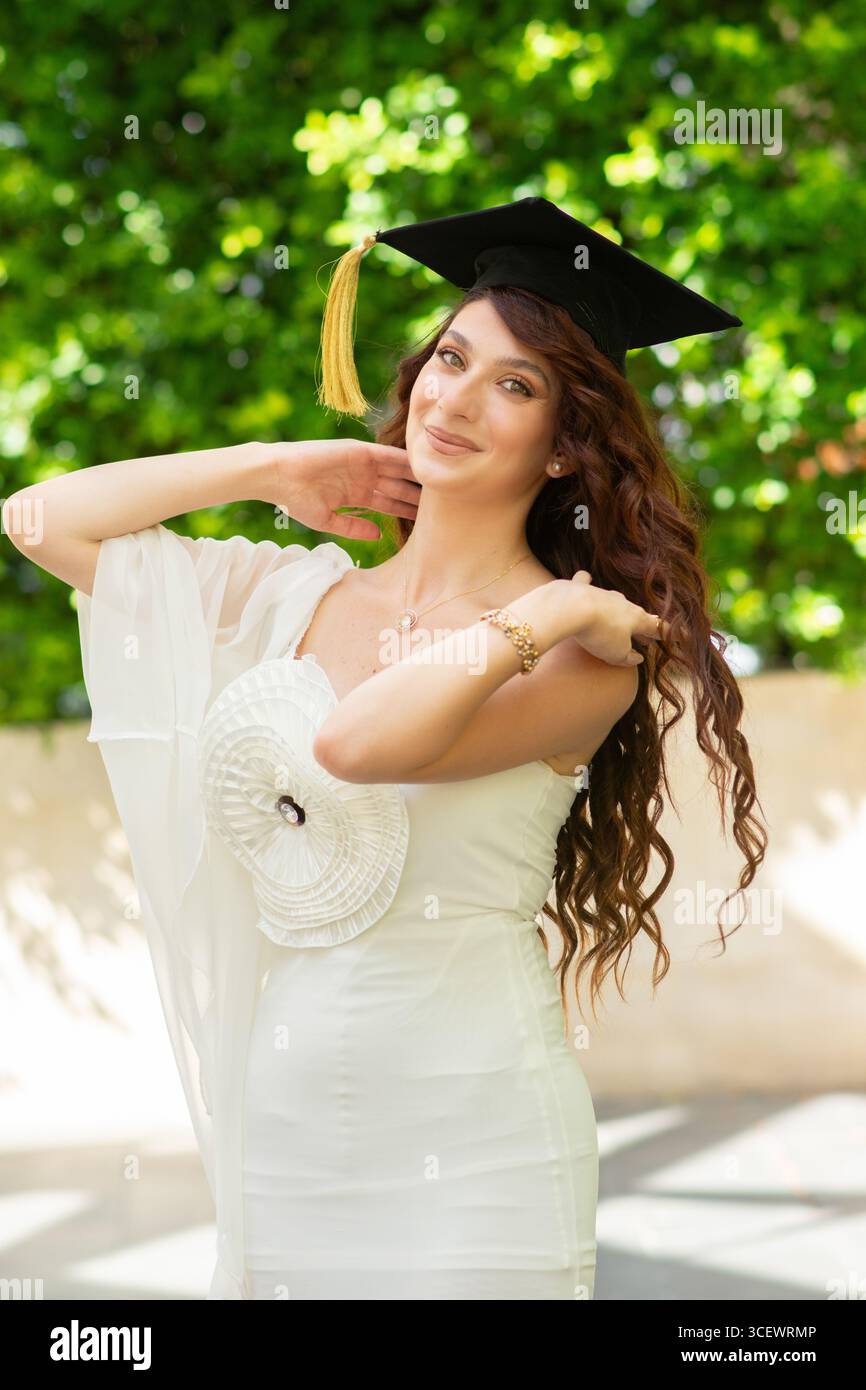 Schöne junge Frau mit weißem Kleid und Abschlussmütze draußen Stockfoto