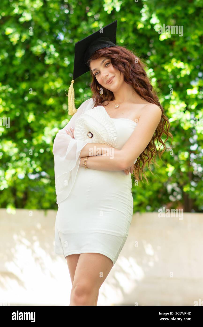 Schöne junge Frau mit weißem Kleid und Abschlussmütze draußen Stockfoto