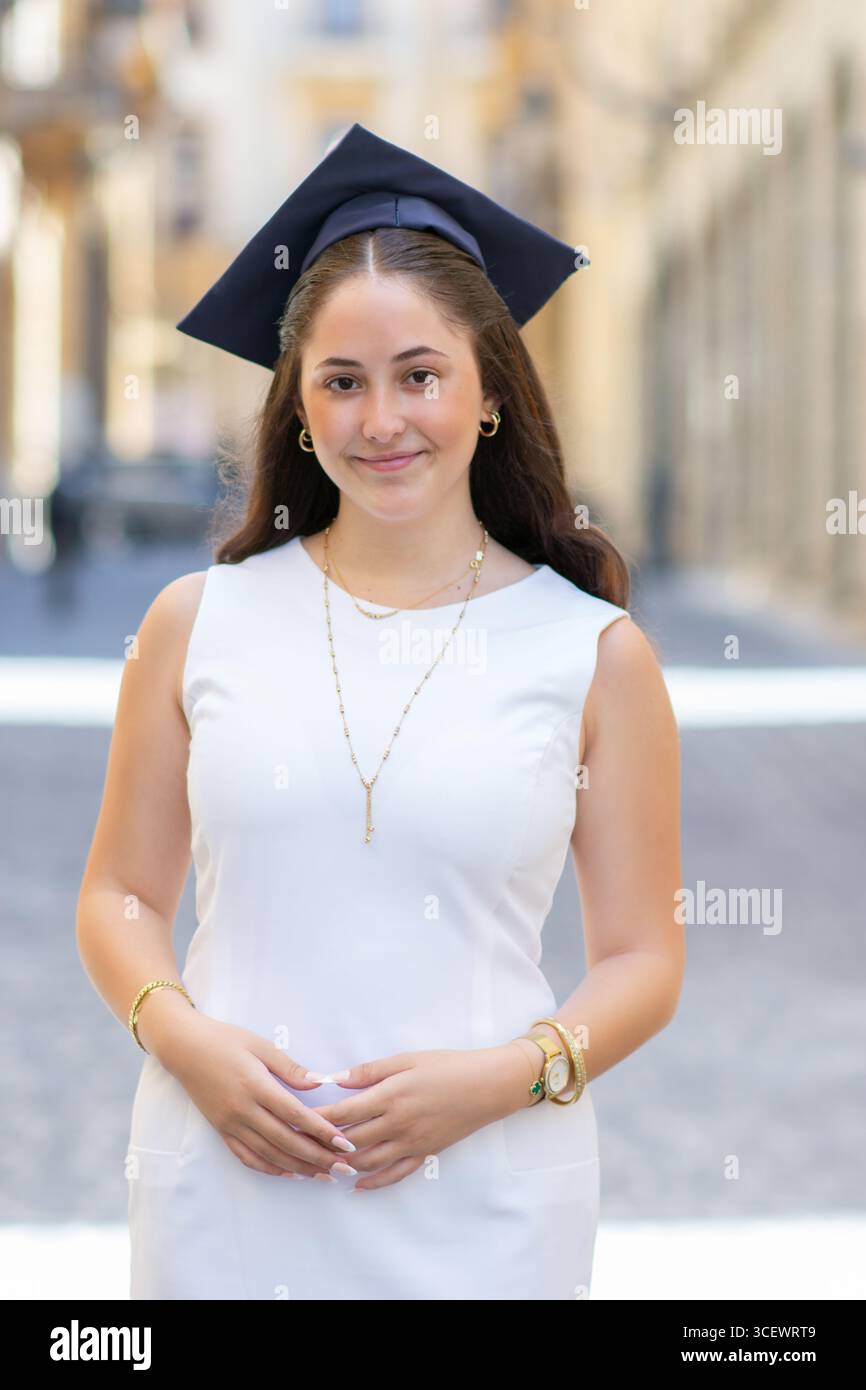 Schöne junge Frau mit weißem Kleid und Abschlussmütze draußen Stockfoto