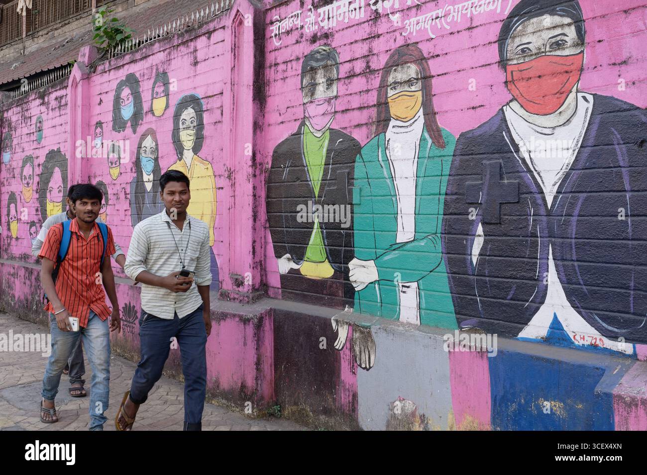 Junge Indianer passieren ein Wandbild aus der COVID-19-Ära in Byculla, Mumbai, Indien, das Menschen mit Schutzmasken darstellt Stockfoto