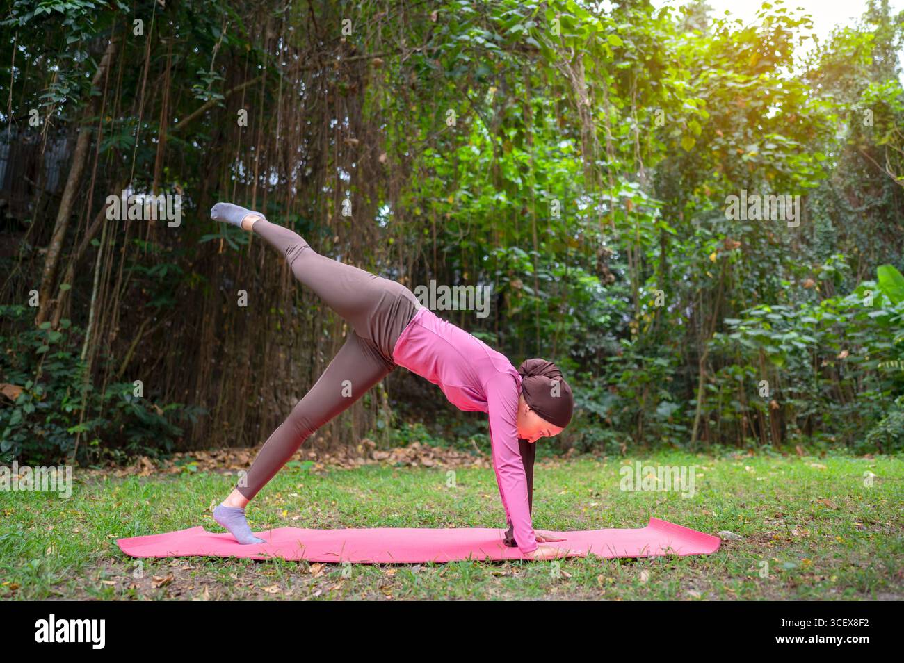 Die indonesische südostasiatische muslimin in einem sportlichen Outfit übt Yoga in einem öffentlichen Park im Freien. Konzept eines gesunden aktiven Lebensstils Stockfoto