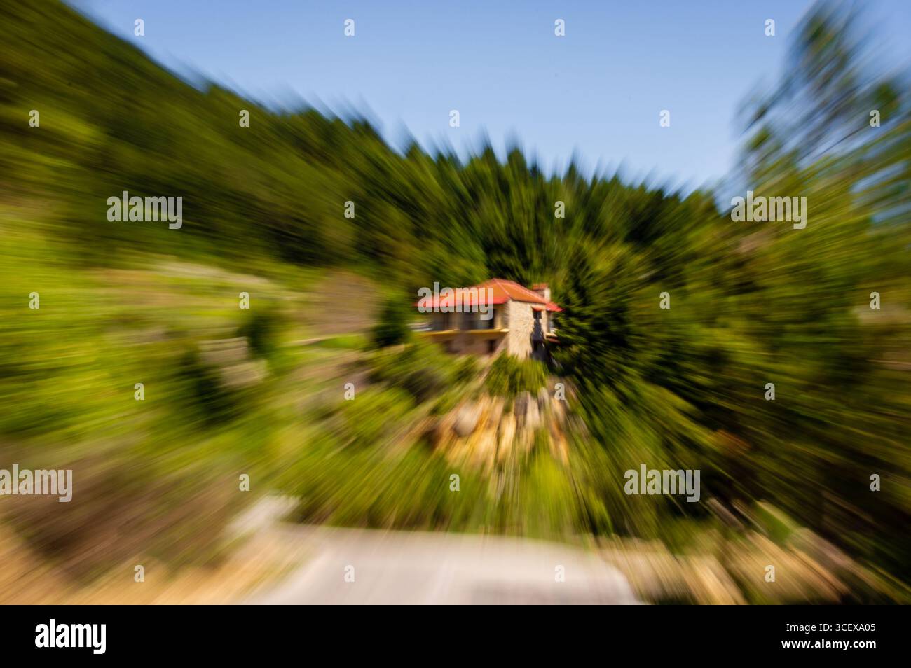 Zoom Unschärfe wird auf ein Steinhaus mit rotem Dach in einem grünen Wald angewendet und erzeugt einen abstrakten Bewegungseffekt. Stockfoto