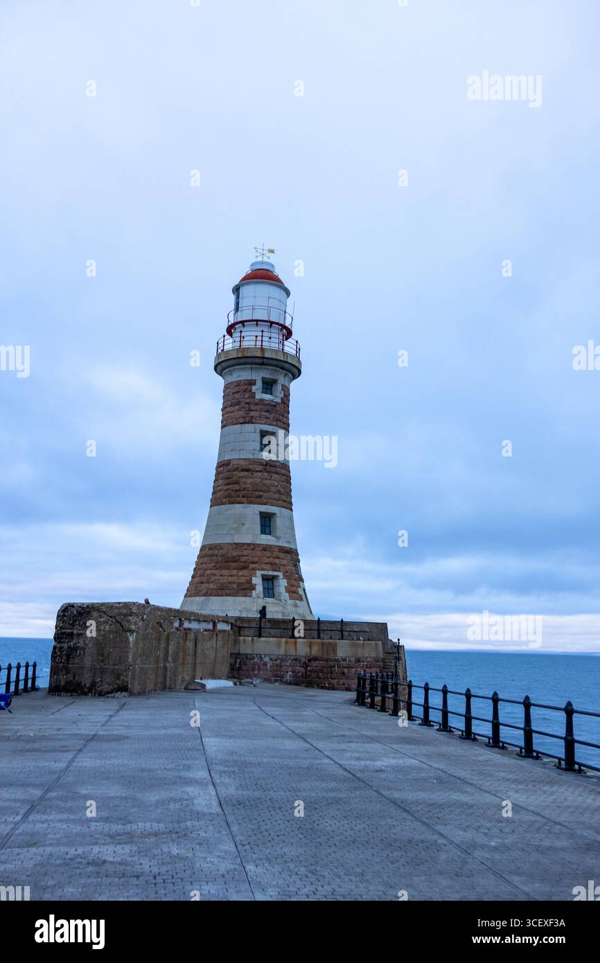 Blick auf einen hohen Leuchtturm aus Stein mit roten und weißen Streifen an der Küste mit Blick auf das Meer unter einem bewölkten Himmel Stockfoto