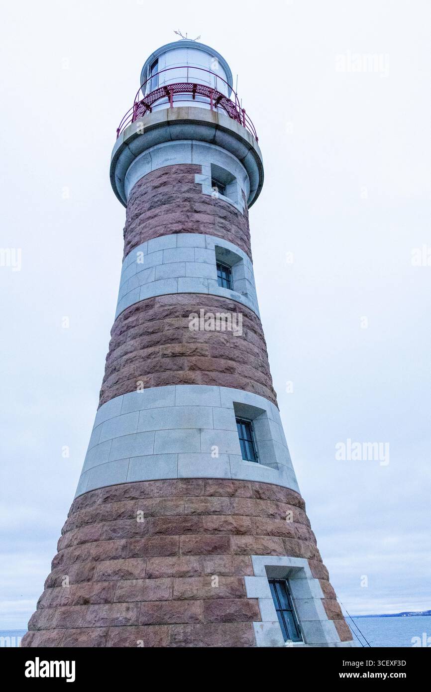 Blick auf einen hohen Leuchtturm aus Stein mit roten und weißen Streifen an der Küste mit Blick auf das Meer unter einem bewölkten Himmel Stockfoto