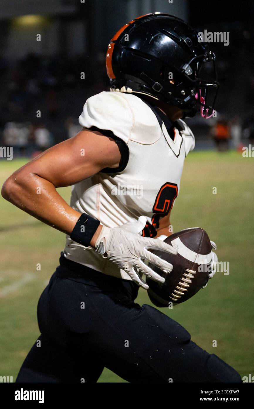 American Football fokussierte Athletin läuft in voller Geschwindigkeit Fußball, die Augen sind im Moment des Outdoor-Spiels mit hohem Einsatz im Auge – purer Grip und Entschlossenheit Stockfoto
