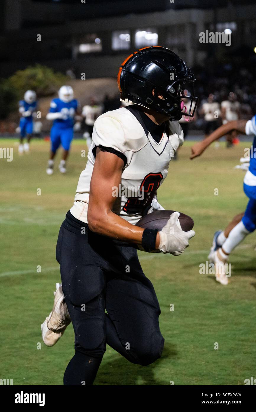American Football fokussierte Athletin läuft in voller Geschwindigkeit Fußball, die Augen sind im Moment des Outdoor-Spiels mit hohem Einsatz im Auge – purer Grip und Entschlossenheit Stockfoto