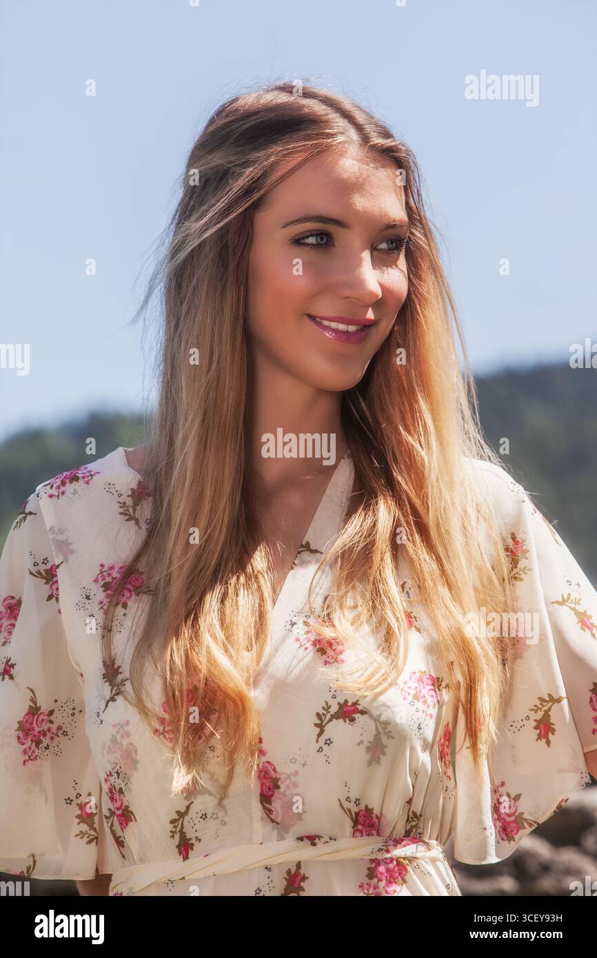 Porträt einer attraktiven jungen Frau mit langen blonden Haaren in einem hellen Blumenkleid. Sie lächelt mit einem natürlichen und frischen Ausdruck, Radiatin Stockfoto