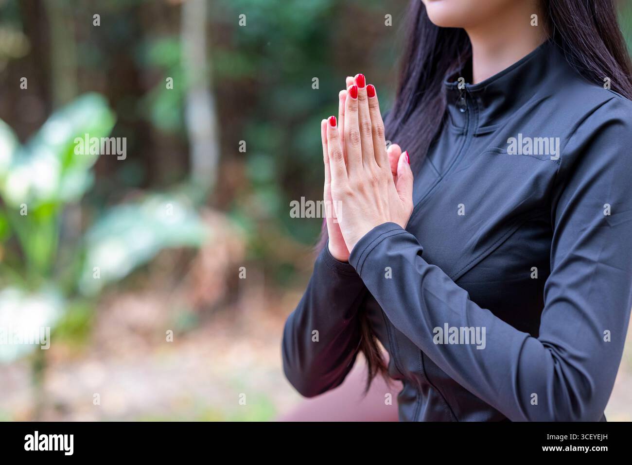 Frau in sportlichem Outfit entspannt sich und meditiert Zen-ähnlich auf einer Fitnessmatte in einem öffentlichen Park im Freien. Konzept eines gesunden aktiven Lebensstils Stockfoto