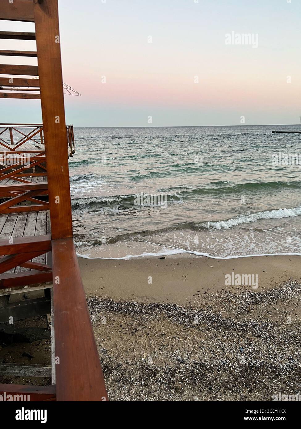 Ein sanfter rosafarbener Sonnenuntergang am Strand des Schwarzen Meeres, der sich vom rosa bis zum blauen Himmel erstreckt - Smartphone-aufgenommenes Stockfoto