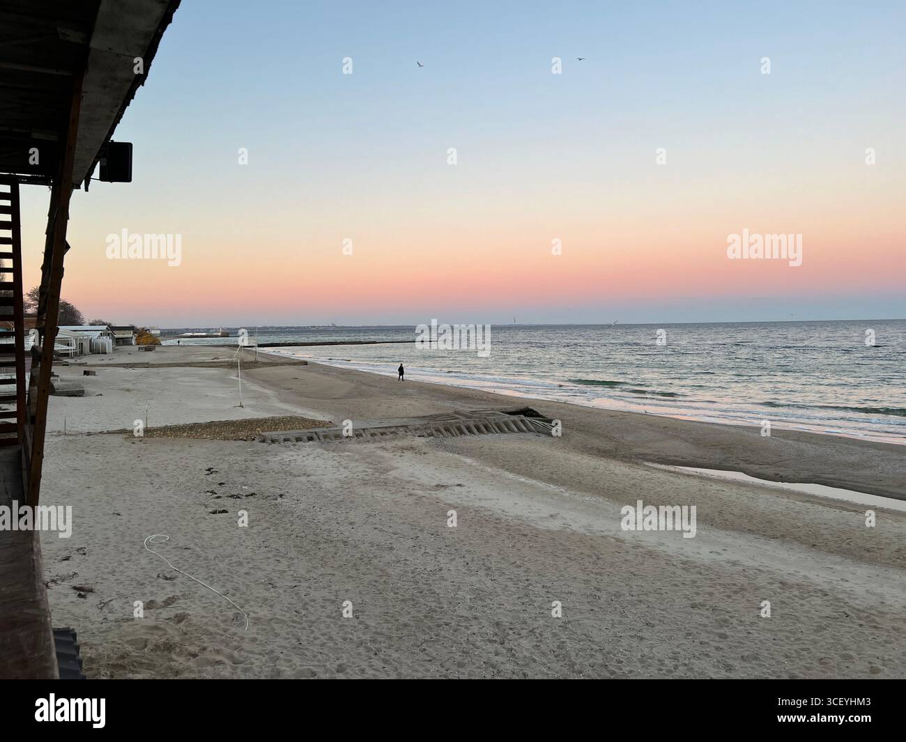 Ein sanfter rosafarbener Sonnenuntergang am Strand des Schwarzen Meeres, der sich vom rosa bis zum blauen Himmel erstreckt Stockfoto