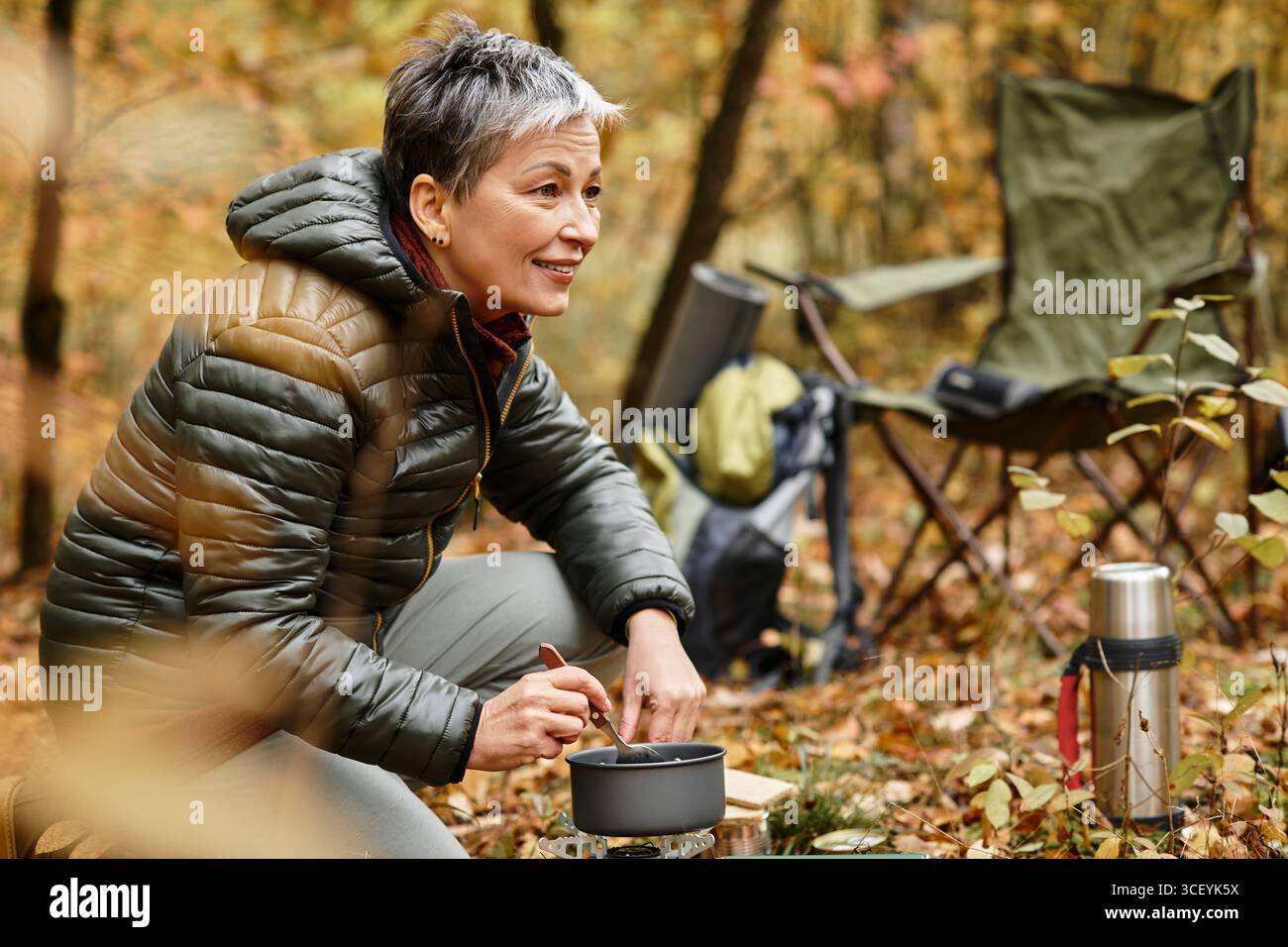 Eine Seniorin kocht gerne im Freien in einem lebendigen Wald und verbindet sich mit Natur und Leben. Stockfoto