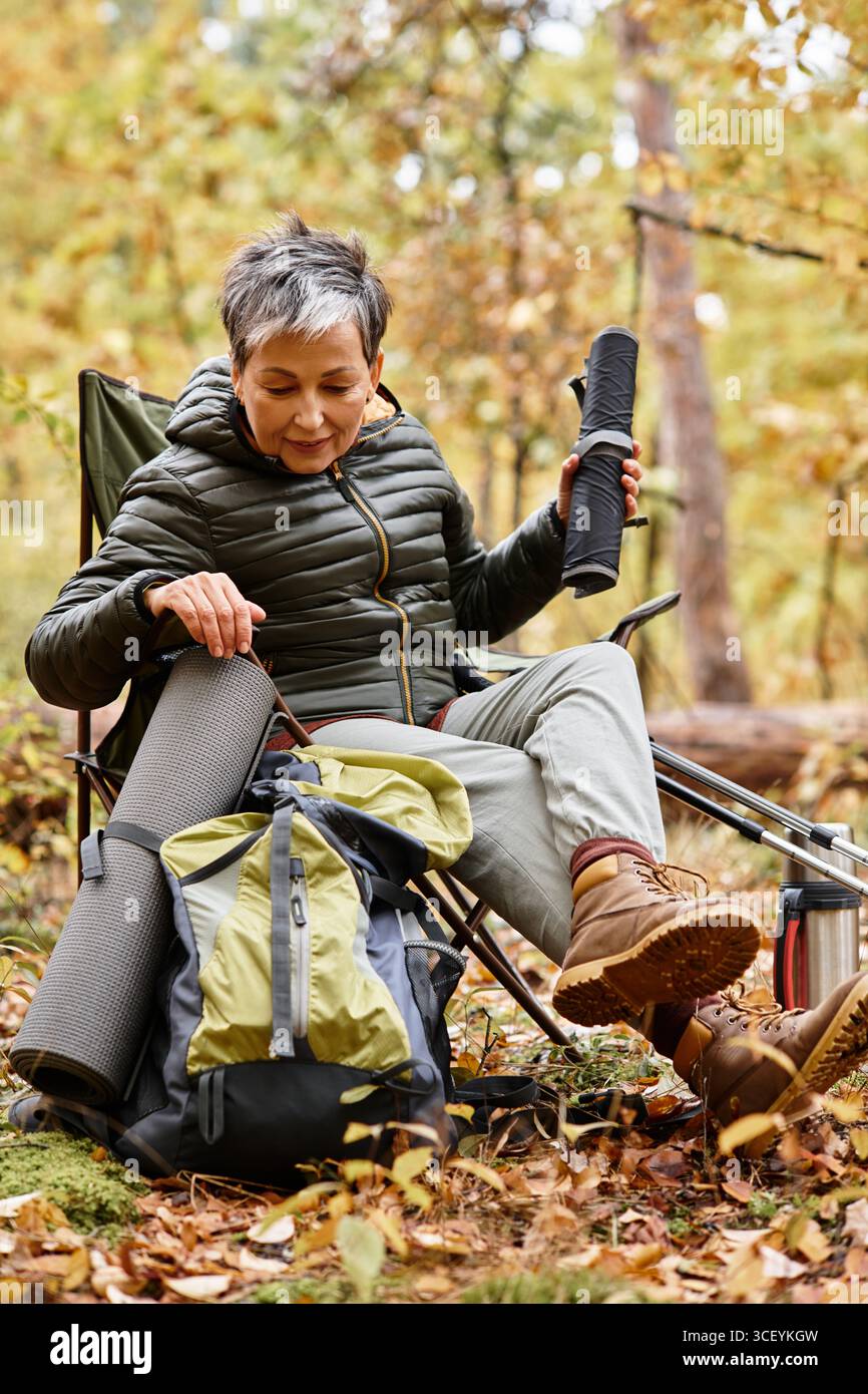 Eine ältere Frau entspannt sich in der Natur und organisiert ihre Ausrüstung nach einer erfrischenden Waldwanderung. Stockfoto