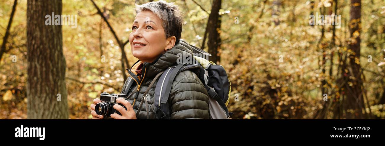 Eine ältere Frau genießt ihre Wanderung im ruhigen Wald und fängt die lebhaften Herbstfarben ein. Stockfoto