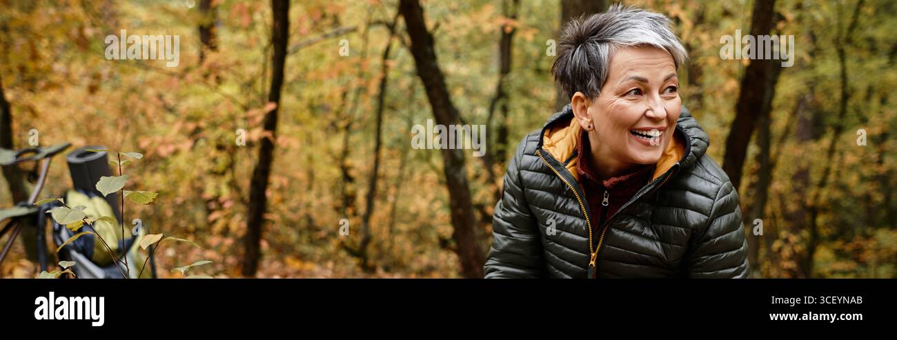 Eine ältere Frau genießt ihre Wanderung in einem bunten Wald, umgeben von Herbstlaub und Ruhe. Stockfoto