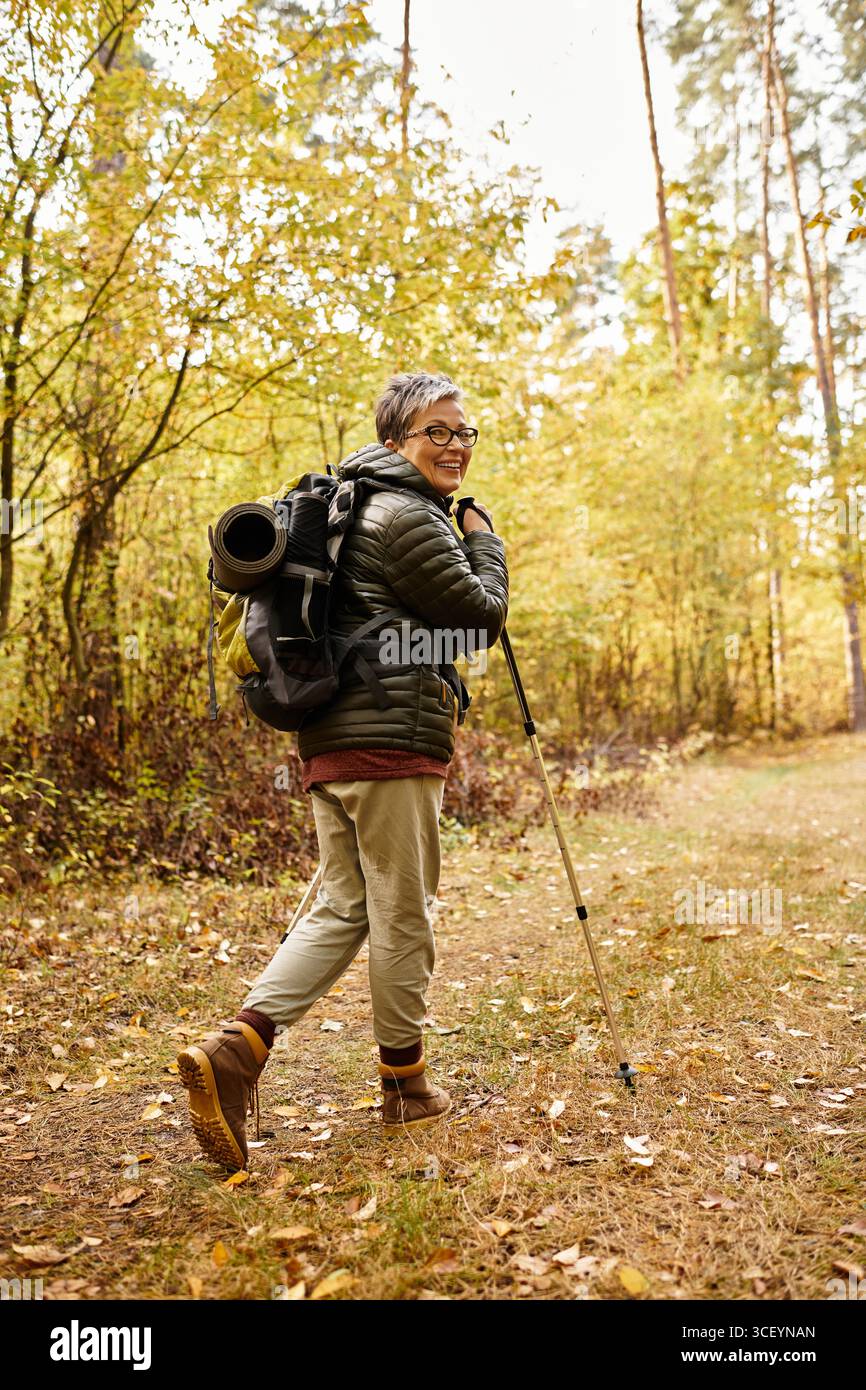 Seniorin genießt eine friedliche Wanderung in den Wäldern, umgeben von Herbstlaub und Naturschönheiten. Stockfoto
