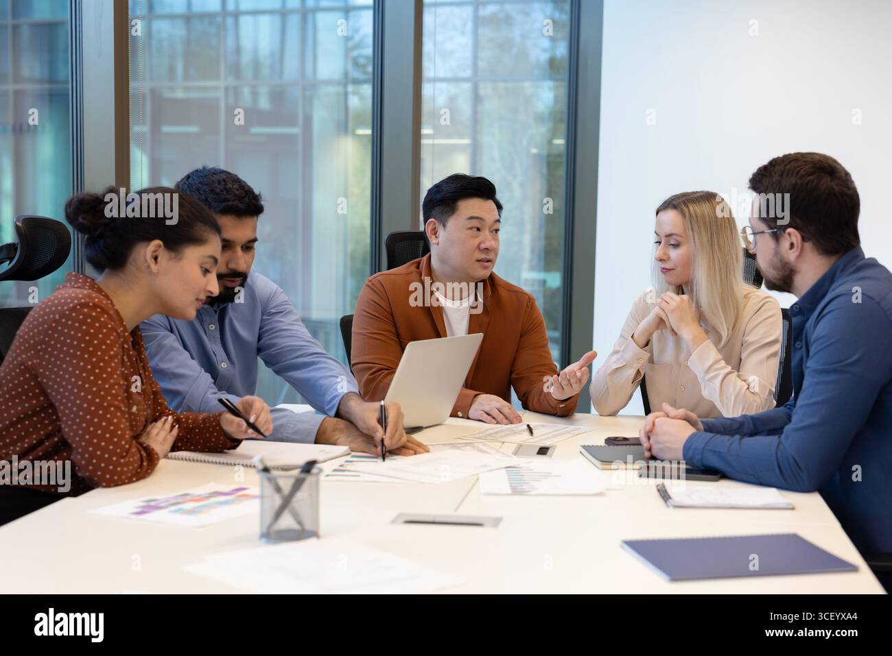 Ein vielfältiges Team von Kollegen arbeitet an Geschäftsstrategien rund um einen Tisch in einer modernen Büroumgebung zusammen und fördert Teamarbeit, Partnerschaft und strategische Planung für erfolgreiche Ergebnisse Stockfoto