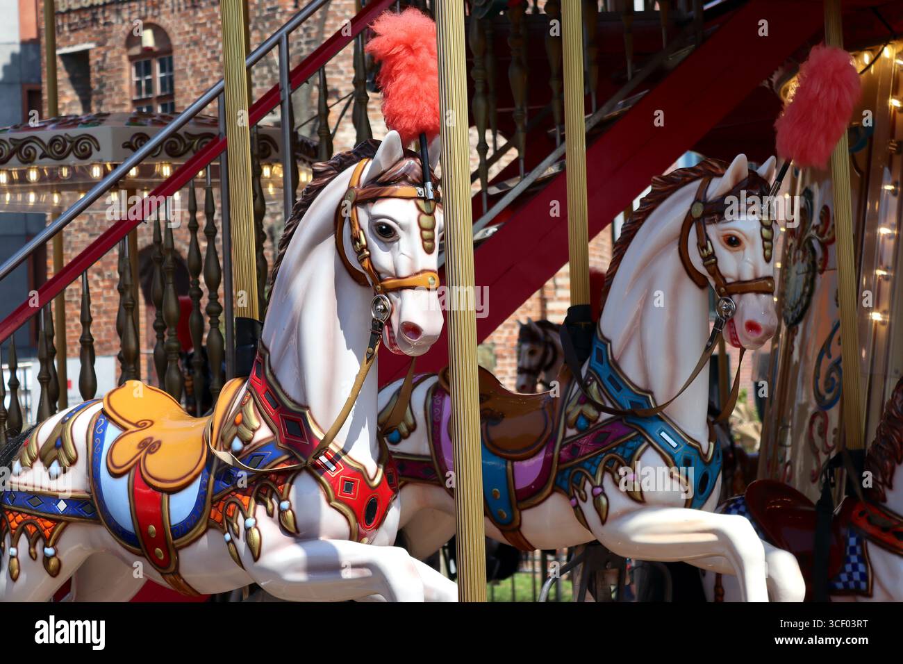 Hell dekorierte Festlandpferde auf einem zweistufigen Karussellritt warten auf Familien, die ihre Pferde bei einem traditionellen Karussellritt in Danzig besteigen. Stockfoto