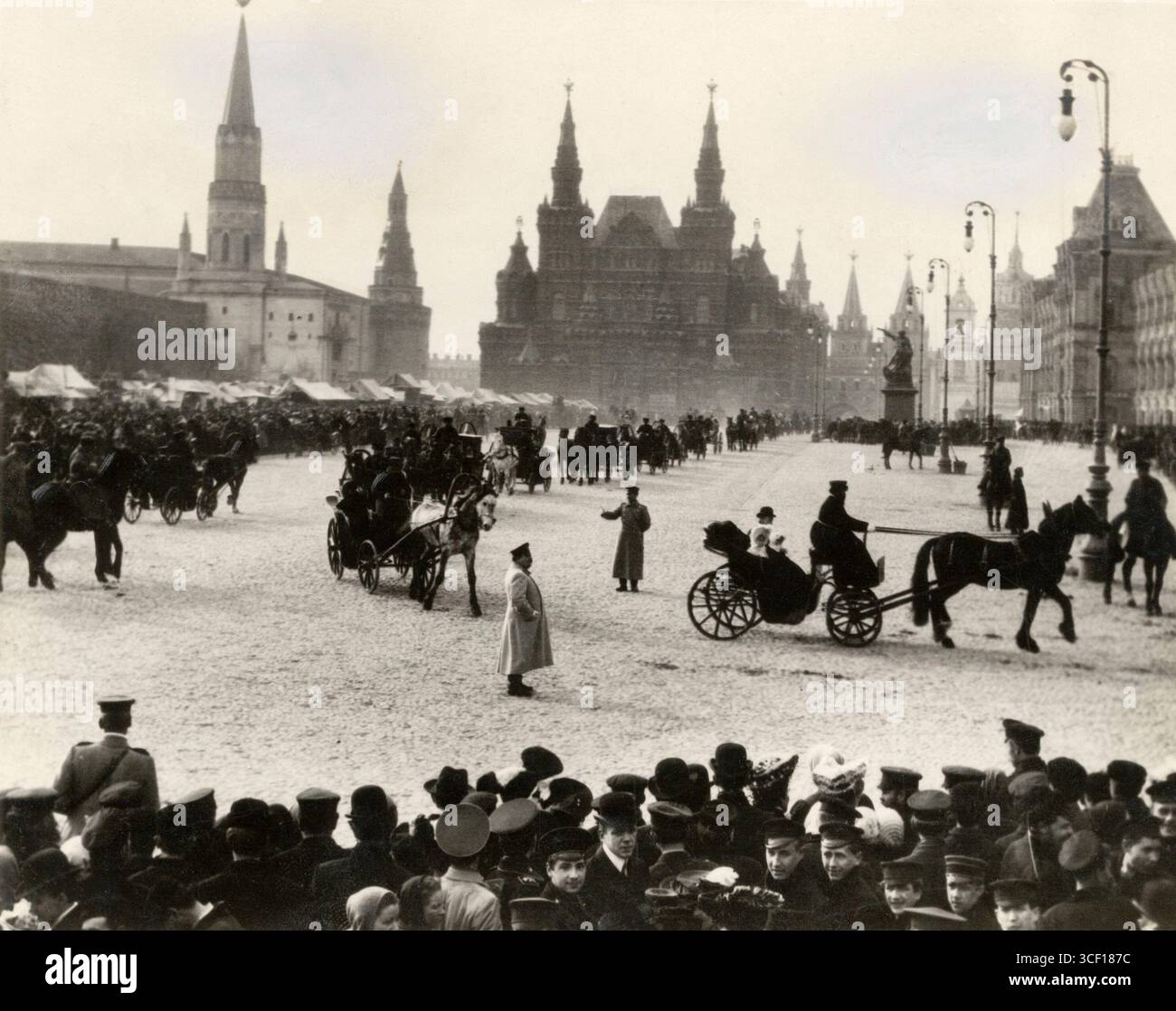 Eine verschneite Szene auf dem Roten Platz in Moskau, wo eine Prozession von Pferdekutschen vorbeizieht. Im Hintergrund befinden sich der Kreml, das nationale historische Museum und Marktstände. Stockfoto