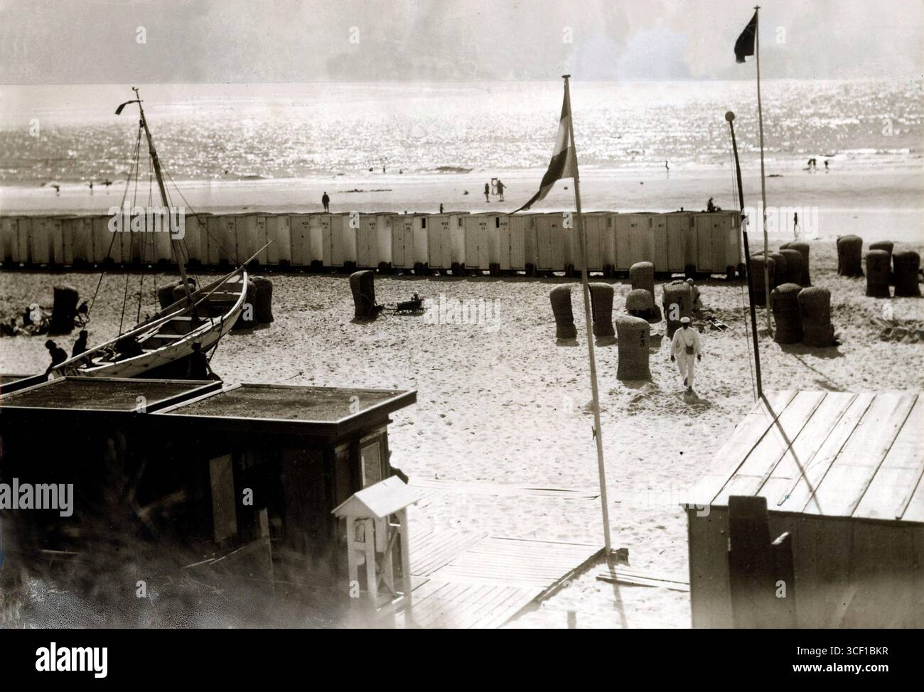 Eine Sommerszene am Strand von Egmond aan Zee, mit Strandhütten auf Rädern, Korbstühlen und einem Fischerboot. Das Bild zeigt das Leben an der Küste der Niederlande im Jahr 1929. Stockfoto