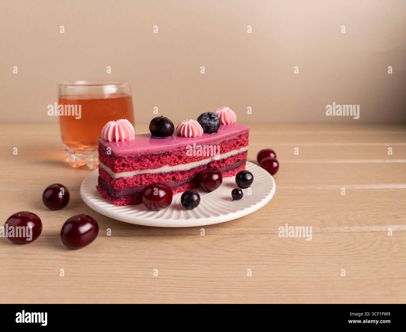 Ein Stück Kuchen mit rosa Zuckerguss und cremiger Füllung. Garniert mit frischen Heidelbeeren und Kirschen, serviert auf einem weißen Teller gegen einen rustikalen Stockfoto