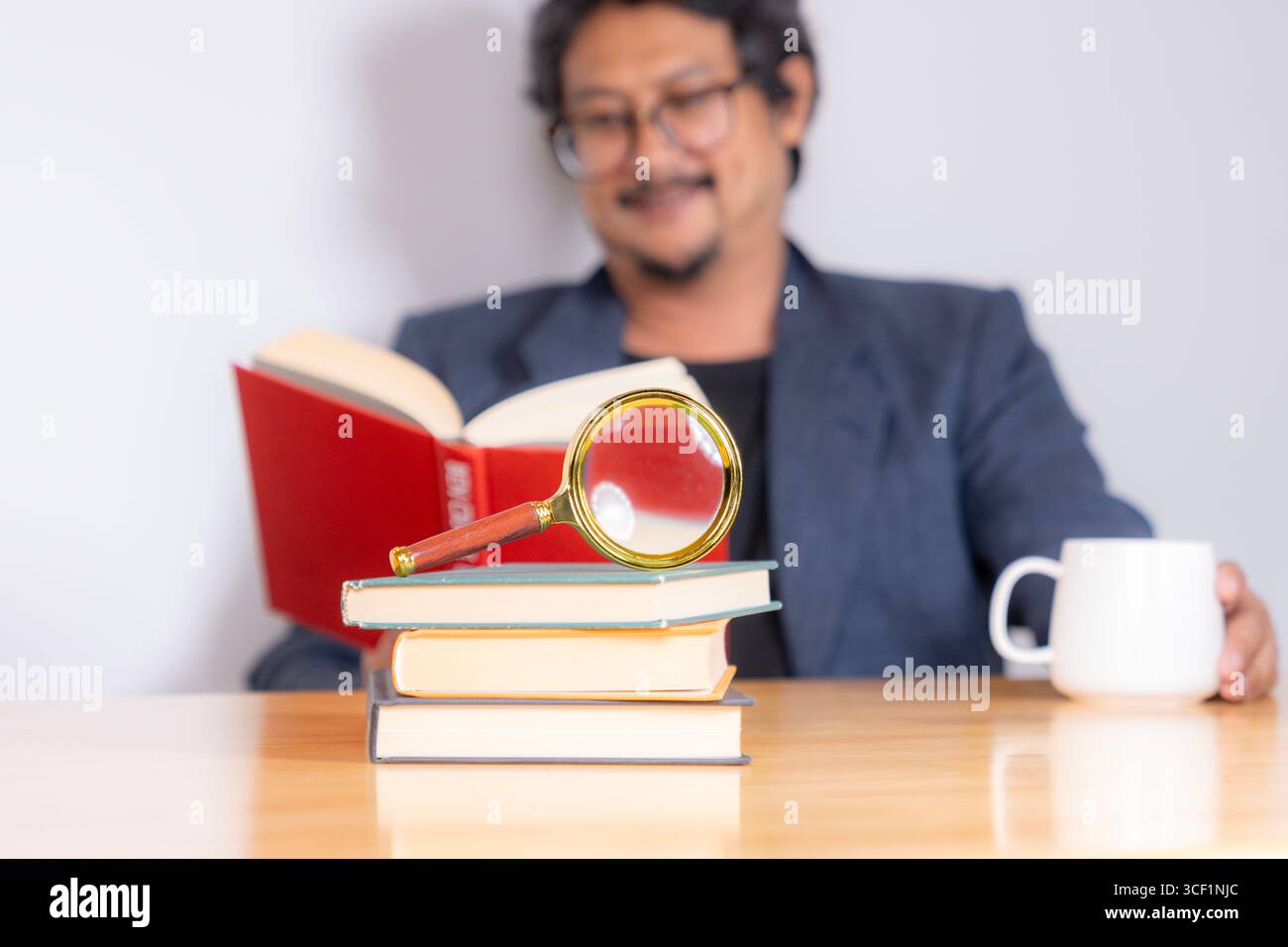 Ein Erwachsener sitzt und liest ein Buch sorgfältig mit einer Lupe, wobei er sich auf Details zum Studium, Wissen oder Forschung konzentriert Stockfoto