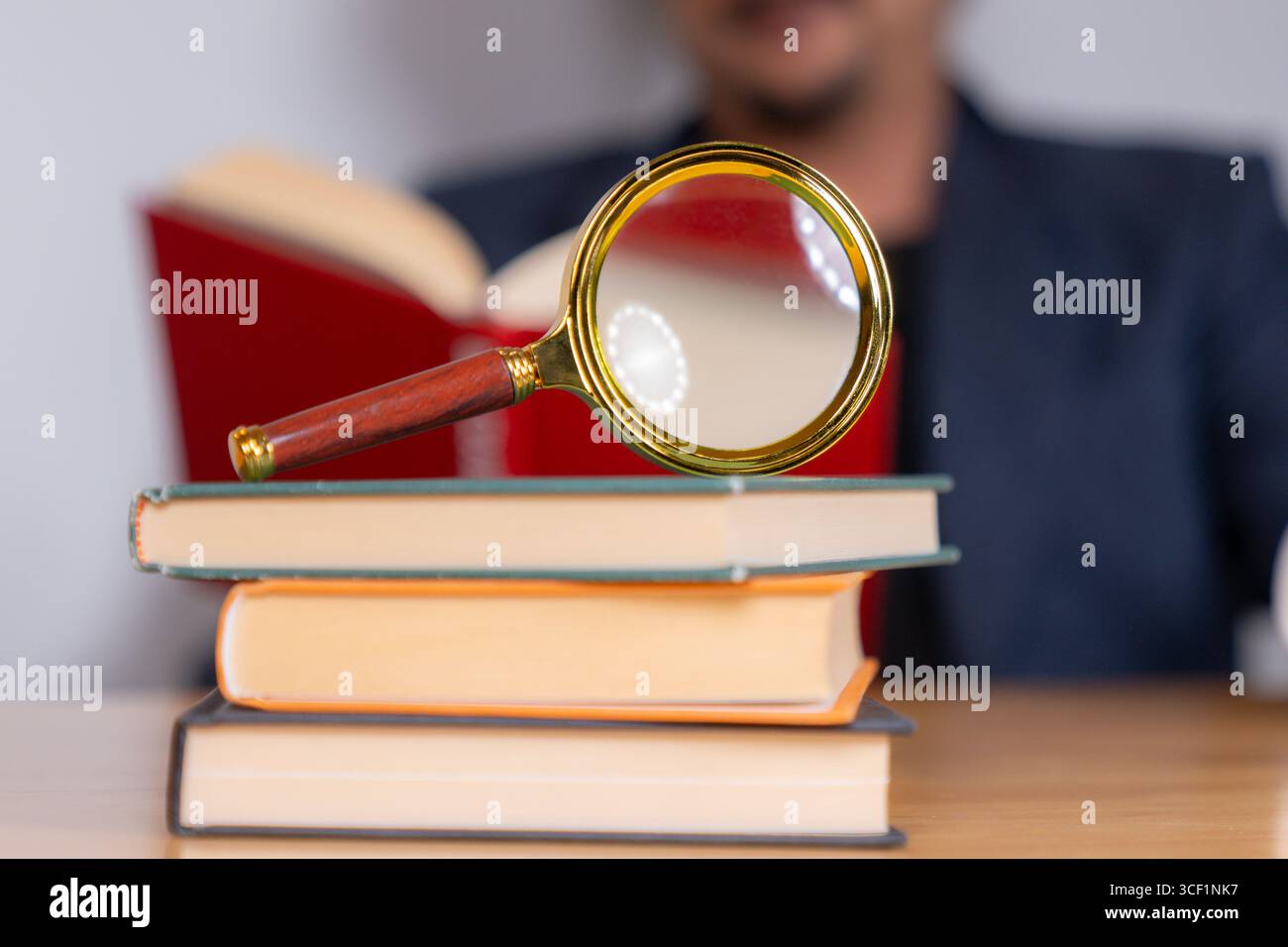 Ein Erwachsener sitzt und liest ein Buch sorgfältig mit einer Lupe, wobei er sich auf Details zum Studium, Wissen oder Forschung konzentriert Stockfoto