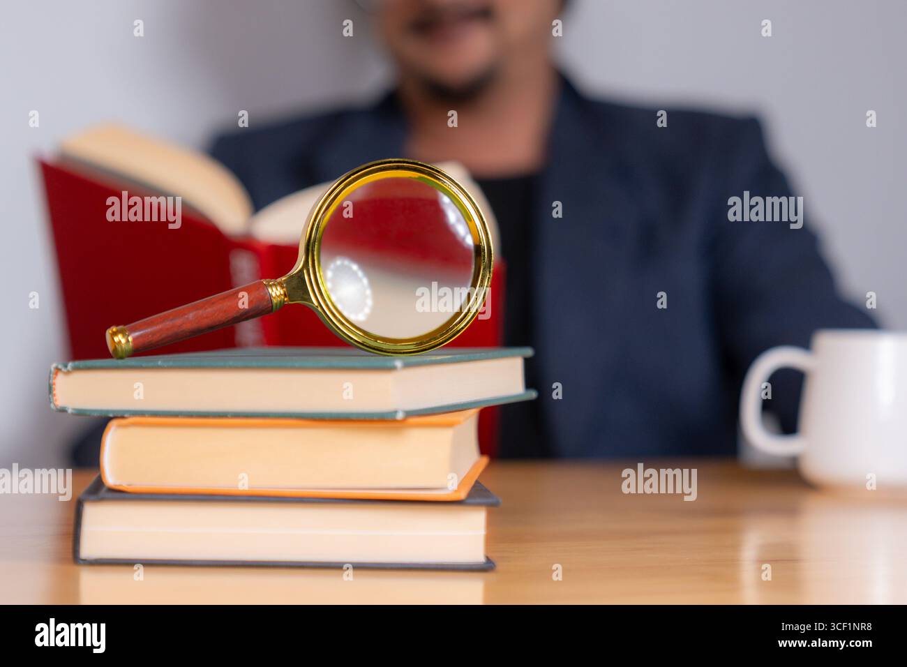 Ein Erwachsener sitzt und liest ein Buch sorgfältig mit einer Lupe, wobei er sich auf Details zum Studium, Wissen oder Forschung konzentriert Stockfoto