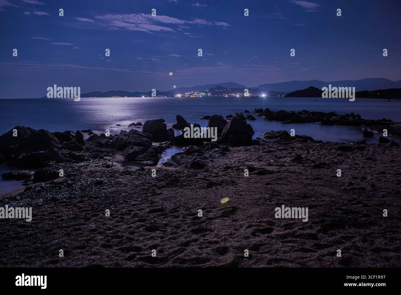 Ruhige Nachtszene am Strand des Capo Ferrato auf sardinien, während der Mond ein sanftes Leuchten auf das ruhige Meer und das felsige Ufer wirft Stockfoto