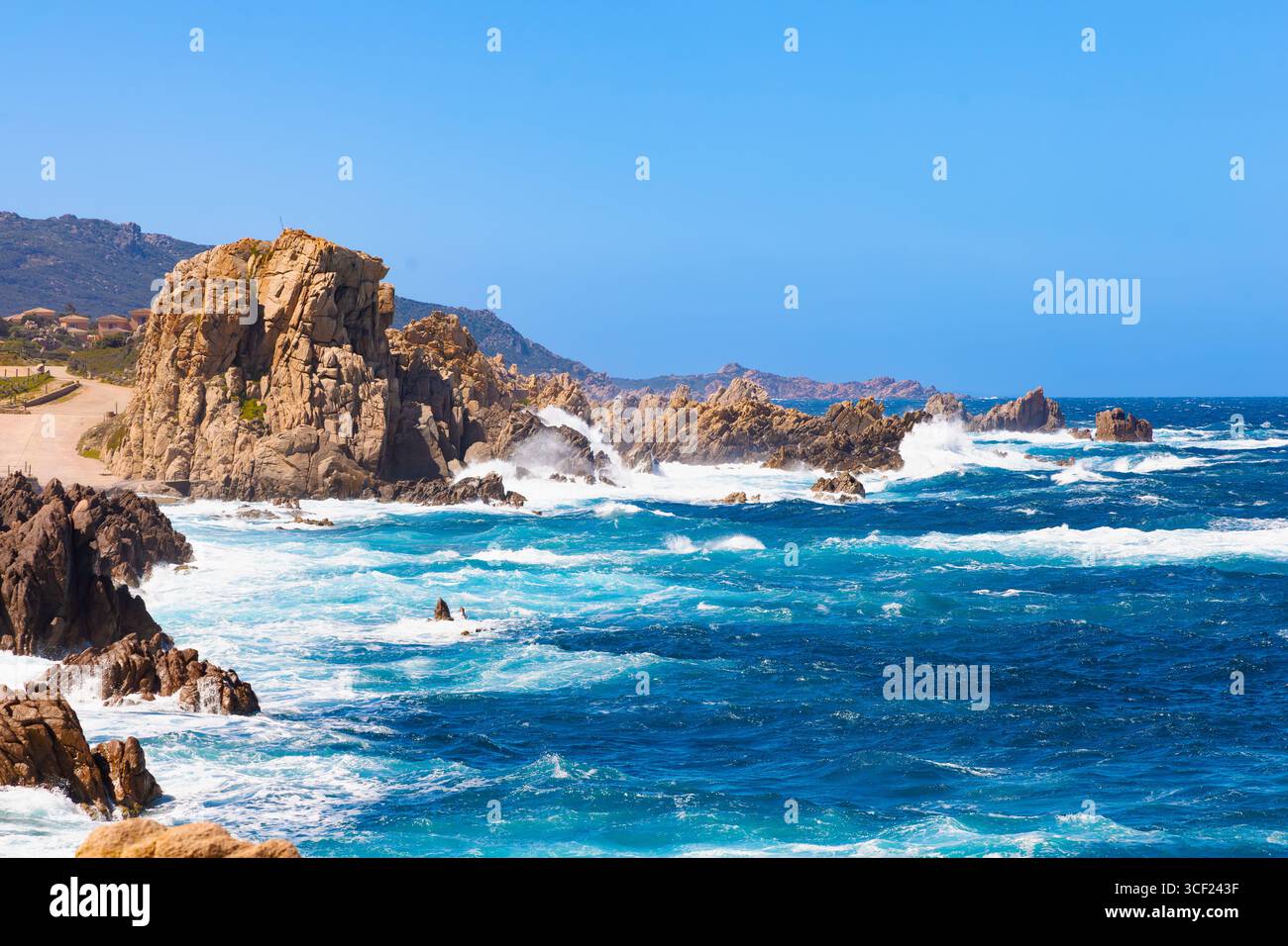 Mächtige Wellen krachen an der zerklüfteten Küste von Costa Paradiso, Sardinien, unter einem leuchtend blauen Sommerhimmel gegen hoch aufragende Felsformationen. Stockfoto
