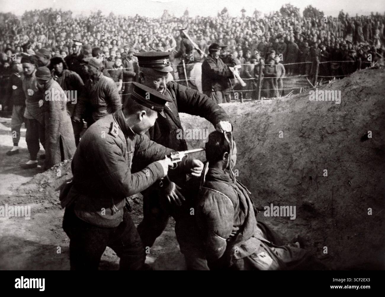 Dieses Foto von 1928 zeigt die öffentliche Hinrichtung eines chinesischen Opiumhändlers in China. Im Rahmen der Anti-Opium-Bemühungen wurden viele Händler zum Tode durch Erhängen verurteilt. Das Bild zeigt, wie der Körper vom Galgen entfernt wird, wobei ein Zuschauer eine Pistole am Kopf der Leiche hält. Stockfoto