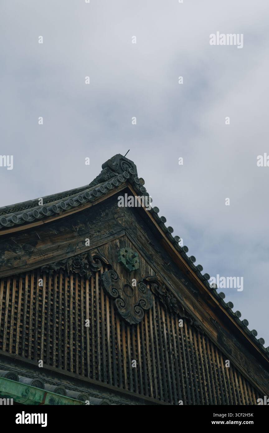 Verwitterter Holzgiebel von Nijo Castle mit kunstvollen Gitterarbeiten unter dem bewölkten Himmel von Kyoto Stockfoto