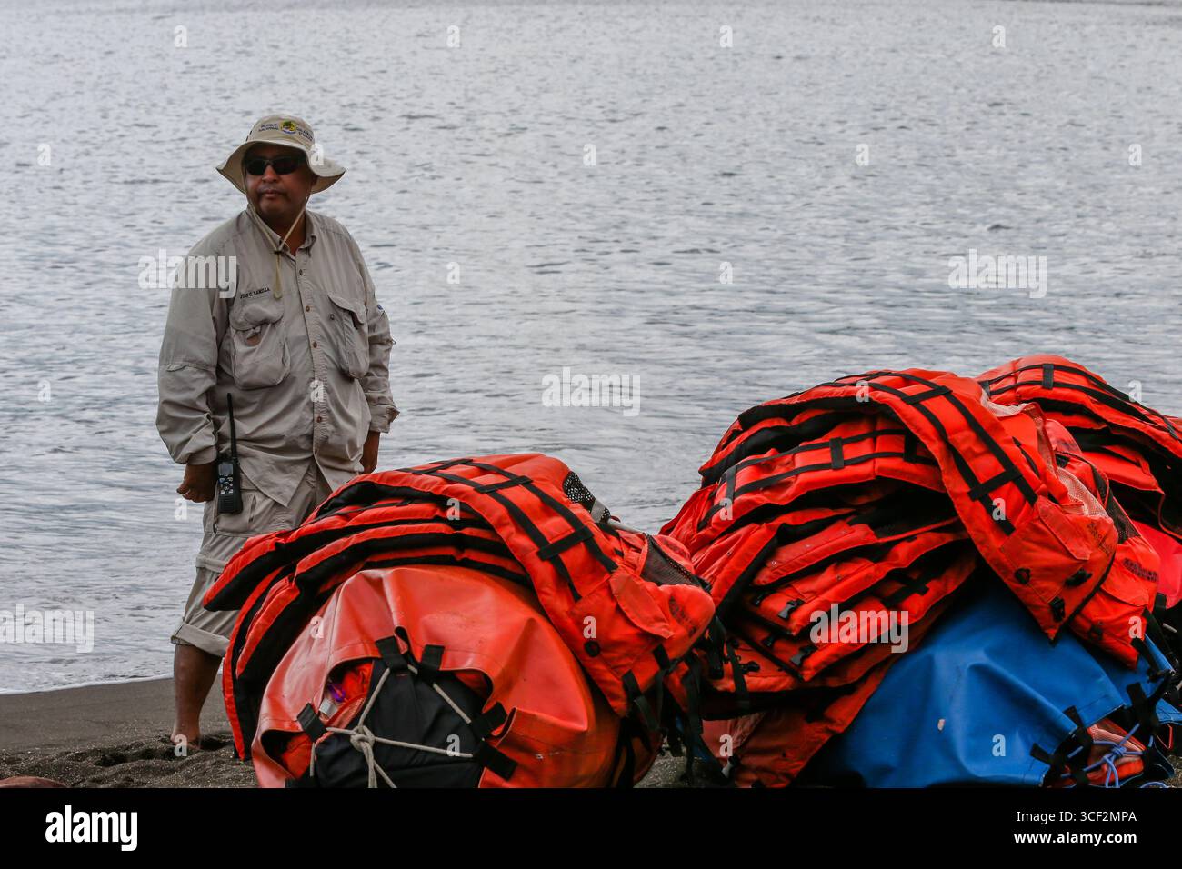 Naturforscher, der neben einem Haufen orangener Schwimmwesten am Ufer der Insel Santiago, der Galápagos-Inseln, Ecuador steht. Stockfoto