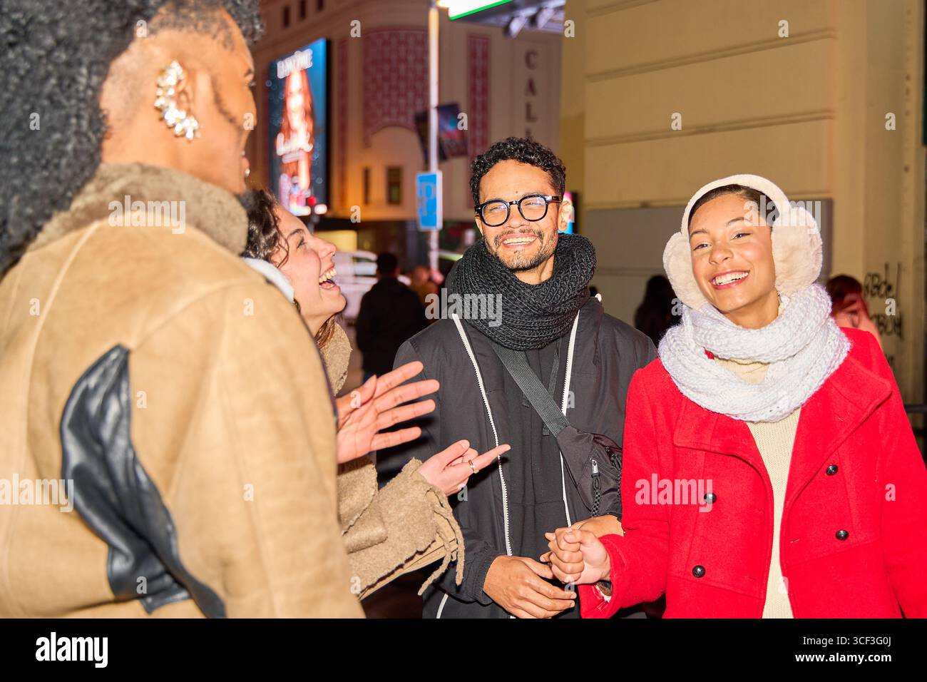 Vier Freunde genießen einen Abend in der Stadt, lachen und unterhalten sich gemeinsam, während sie eine geschäftige Straße hinunterlaufen Stockfoto
