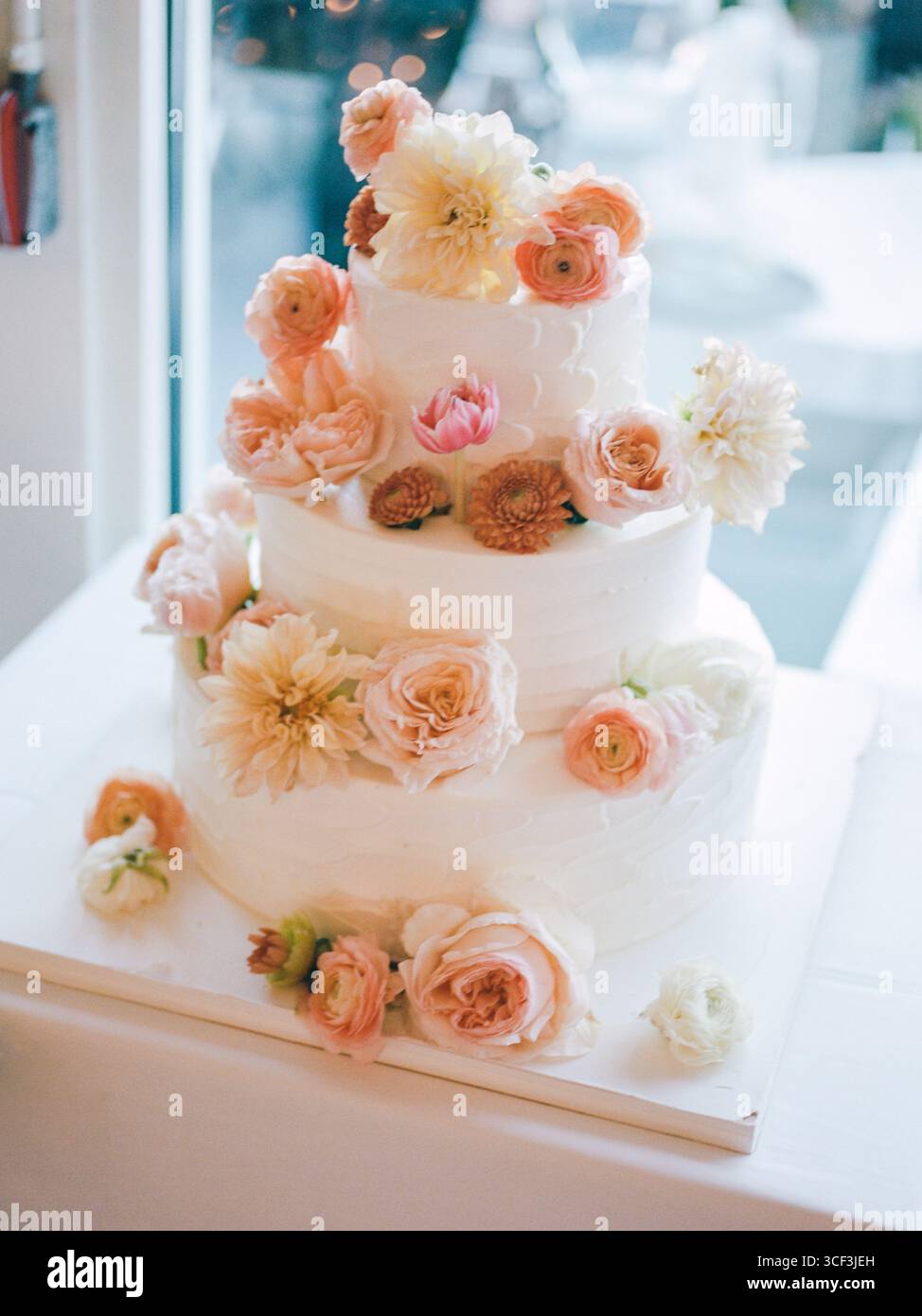 Eine atemberaubende dreistufige Hochzeitstorte mit zarten Blumendekorationen in einem hellen Rezeptionsbereich. Stockfoto