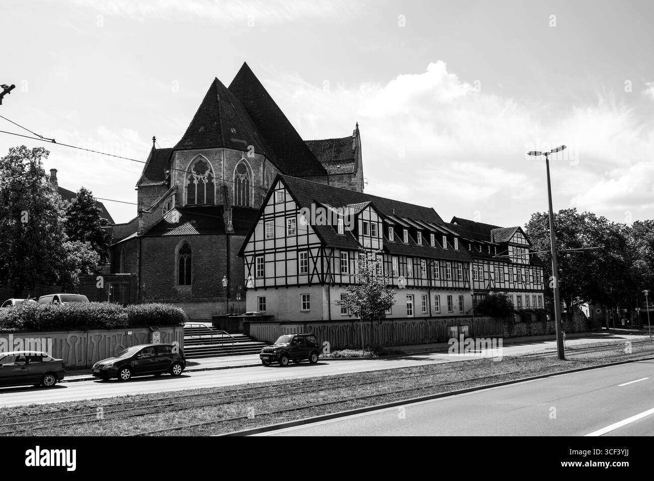Ein dramatisches Schwarzweiß-Foto einer gotischen Kathedrale mit spitzen Dächern neben historischen Fachwerkhäusern in einer europäischen Stadt. Stockfoto