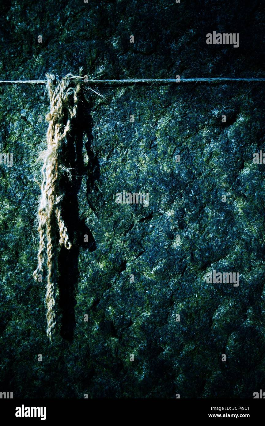 Ein straffer Faden mit Resten einer Schnur vor einer Steinmauer Stockfoto