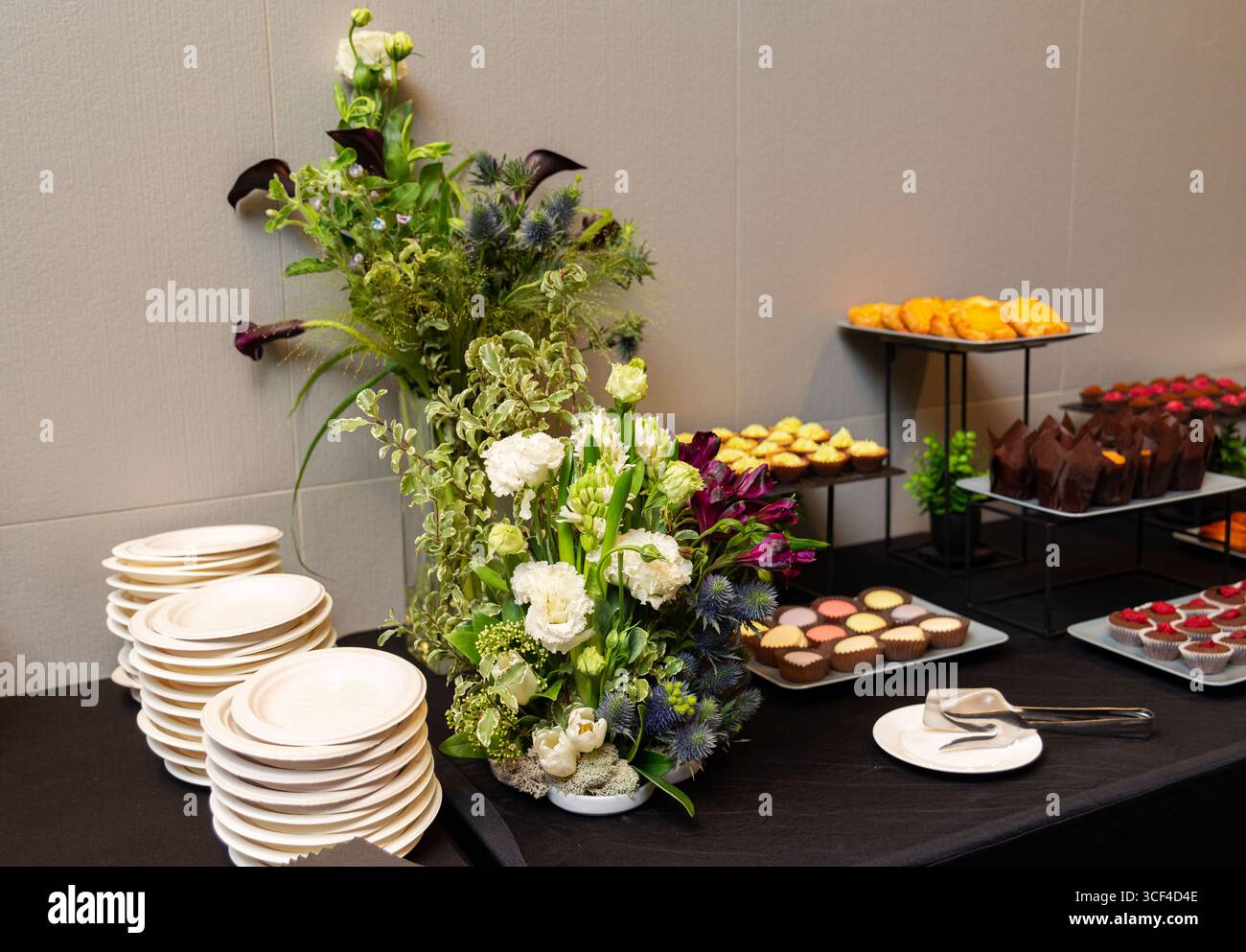 Ein wunderschön gestalteter Veranstaltungstisch mit Blumenmotiv, umgeben von verschiedenen Desserts. Die Einrichtung umfasst Teller und elegantes Besteck, Stockfoto